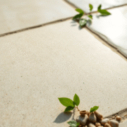 Close-up of a polished stone floor with glossy finish, reflecting soft natural light, surrounded by small pebbles and green leaves.