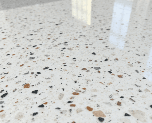 Close-up of a polished terrazzo floor with colorful marble and glass chips in a smooth, shiny surface under soft natural light.