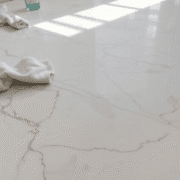 Close-up of polished marble floor with natural veins, sunlight highlighting its shine, and a soft cloth with pH-neutral cleaner nearby.