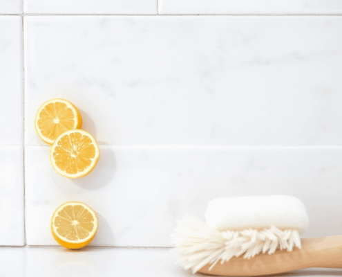 Close-up of shiny bathroom tiles with bright grout, lemon slices, baking soda, and a soft brush in a bright, airy bathroom.